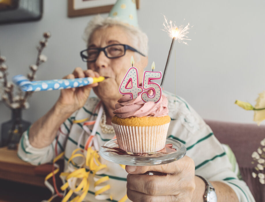 Older adult celebrating Day Brook Village’s 45th anniversary with a cupcake and party horn.